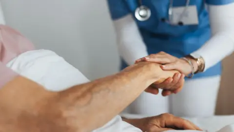Getty Images A nurse holding the hand of a patient in bed