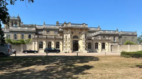 Mousumi Bakshi/BBC The outside of Shrubland Hall, which is a historic English country house. The sky is blue with no clouds.