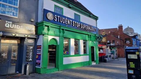 A green and white fronted building with a black sign that says "Student Stop Supermarket"