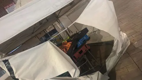 Tommy Coyle The fruit stall has been vandalised in this image. The veg trays have been scattered and the white canopy has been slashed. 