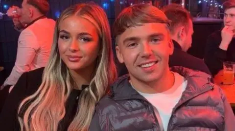 Olivia Allsopp A young couple, a woman with long wavy blonde hair wearing a black top, and a man with short blonde hair, a white t-shirt and grey padded jacket.