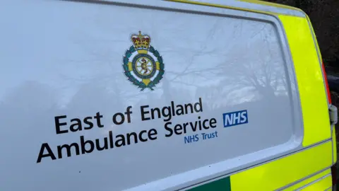 A close-up of the side of an East of England Ambulance Service vehicle. The service's emblem is above the words "East of England Ambulance Service".