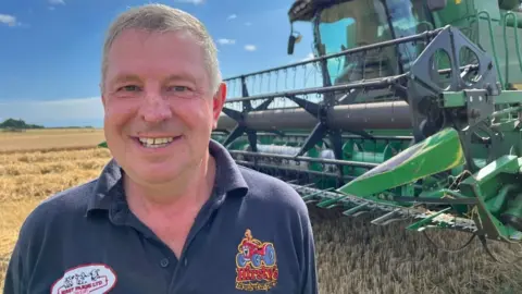 Andrew Turner/BBC A smiling Richard Hirst standing next to a combine harvester