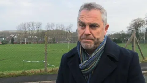 BBC Elwyn Vaughan MS standing outdoors near a large open sports field