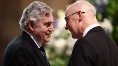 PA Media Gordon Brown, on the left of the shot with grey hair, and John Swinney, bald with glasses, talk while standing close to each other 