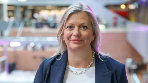 Hayley Valentine in a blue suit jacket with a gold chain