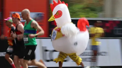 EPA/Shutterstock A runner dressed in a large, white inflatable chicken costume with a red comb and yellow beak navigates the marathon route.