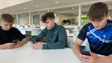 BBC Three male pupils looking at their phones waiting for exam results