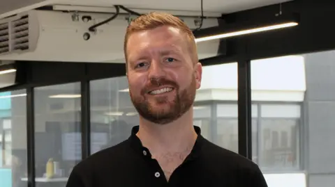 FourJaw A smiling Chris Iveson wearing a black polo shirt looks straight into the camera.
