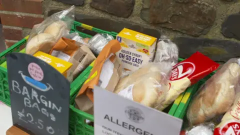 Two green boxes containing food, including instant porridge, bread and all sorts of different packets of pastries. There is a blackboard sign and it reads: 'Bargain Bags £2.50'.