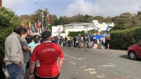 Para pengunjuk rasa berkumpul di luar Hotel Stradey Park di Llanelli ketika rencana untuk menggunakannya sebagai perumahan sementara bagi pencari suaka diumumkan.  