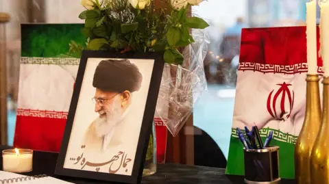 A portrait of Iran's Supreme Leader Ayatollah Ali Khamenei is displayed next to Iranian flags, candles and a book of condolences at a mosque in Cape Town