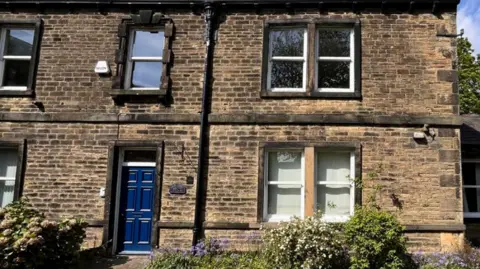 A terraced house of stone with a blue door and windows on each of the two storeys.