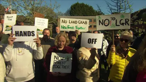Crowds of people stood with signs outside the New Forest District Council offices. Some signs read "hands off", "new forest together", "no land grab".