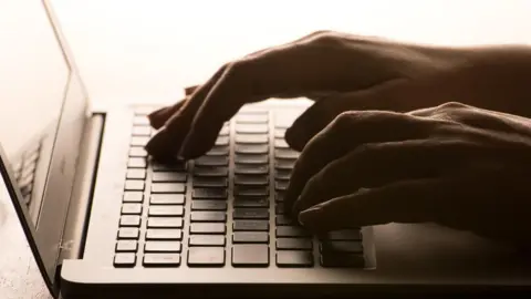 PA Media Two hands, darkly lit, using a laptop keyboard.