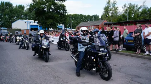 Jacob King/PA Wire Bikers travel through the street while crowds line the side of the road