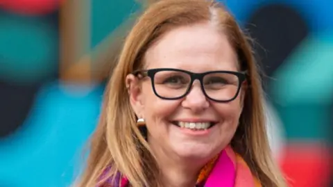 Headshot of Helen Godwin. She is smiling while wearing black-rimmed glasses and a pink and orange scarf.