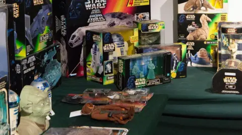 Duggleby Group A collection of Star Wars memorabilia, including action figures and models of a variety of space vehicles. The items are on a green table. 