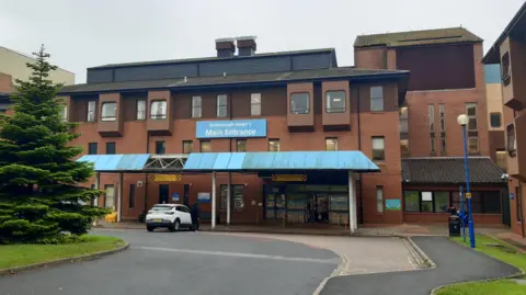 Anttoni James Numminen Scarborough hospital a modern red brick building with brown wooden window frames and a blue covered porch area