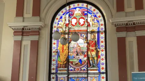 GUY CAMPBELL/BBC A large, colourful stained glass window in the former council chamber showing a depiction of St George 