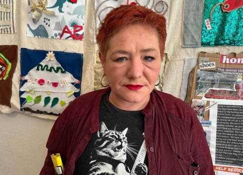 Annie stands in front of art work wearing gold earrings, red lipstick, a black and white T-shirt with a cat on it