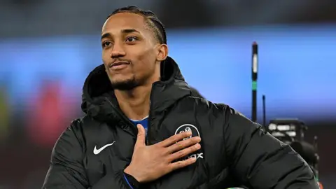 Joao Pedro pats the Chelsea badge while facing towards chanting fans
