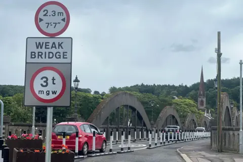 Cars make their way across a bridge lined with bollards and a sign flagging up the three tonne weight restriction