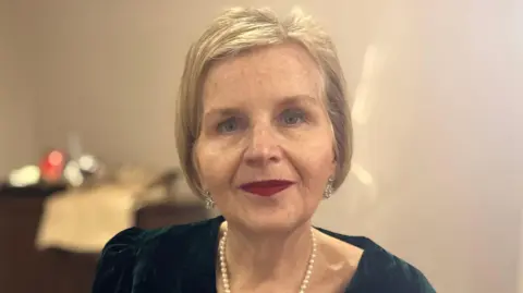 A profile of Donna Ockenden wearing a green velvet dress, a pearl necklace and silver earrings