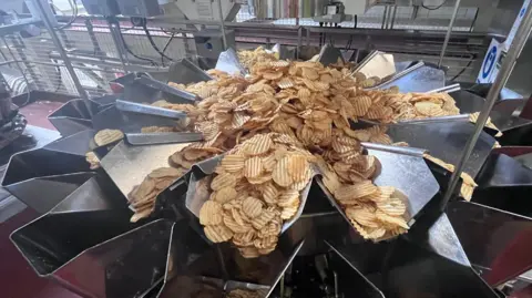 Abigail Jaiyeola/BBC A pile of crisps are sorted into different drums to be seasoned.