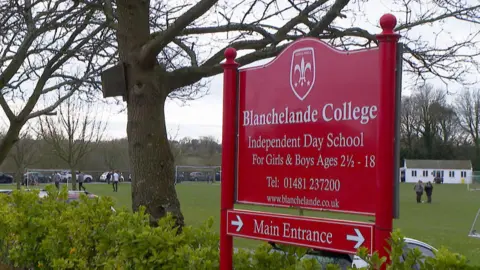 A red sign for Blancheland College showing a fleur de lis crest. Children are seen playing in a field in the background. 