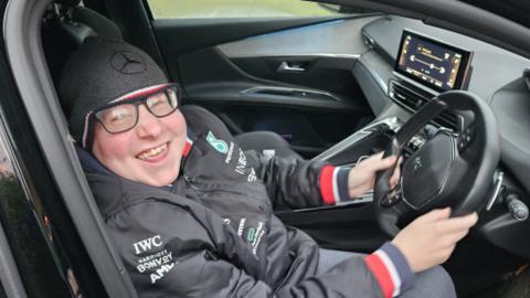 Shaun Cooke smiling as he sits in the driver's seat of a car