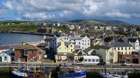 MANX SCENES A range of properties in the seaside town of Peel. Boats moored in the inner harbour can be seen in the foreground, with buildings behind them stretch out into the distance. 