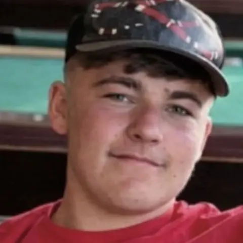 Family handout The photo shows Ethan Slater in a red t-shirt and a black cap. He has brown hair, and is smiling at the camera. 