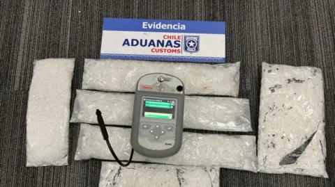Chile Aduanas Customs Bags of white powdery substance laid on the floor, with some sort of testing device placed on top of it. Above the photo is a card which says 'Evidencia, Chile Aduanas Customs'.