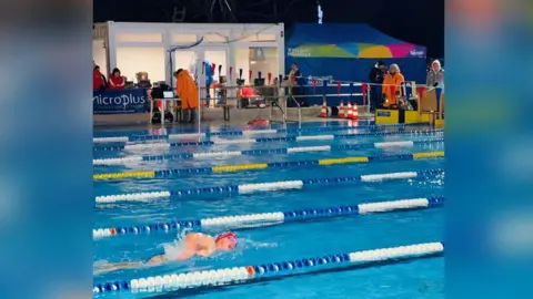 Handout Helen Hislop is swimming while a number of people at the side of the pool are wrapped up against the freezing weather, wearing coats and hats.