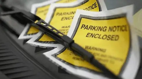 Three yellow parking tickets, sit under a black metal pole, on top of a black platform.