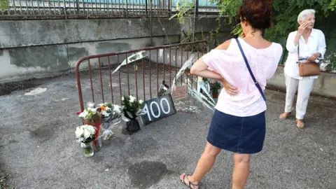 AFP Women look at a display of flowers as they stand at the site where a woman was found dead the day before, in Cagnes-sur-Mer on 2 September 2019, making her the 100th victim of femicide in France this year