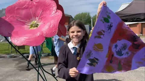 Andrew Turner/BBC Rosie holding a flag, next to a giant flower