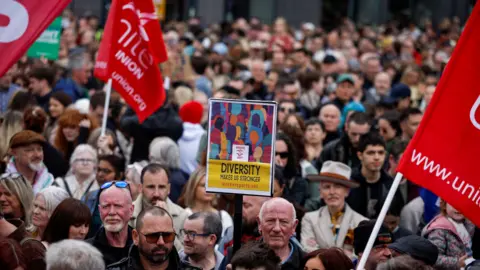 Reuters A large crowd stands at City Hall holding up placards and flags, including Unite the Union.