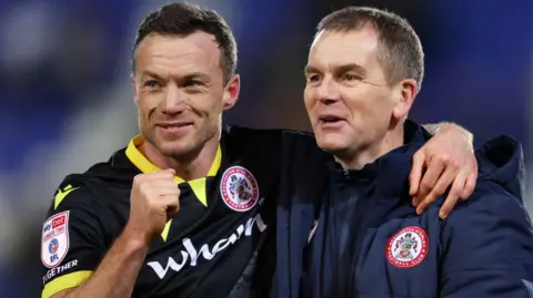 Shaun Whalley with right first clenched and his left arm around the shoulder of Accrington boss John Doolan