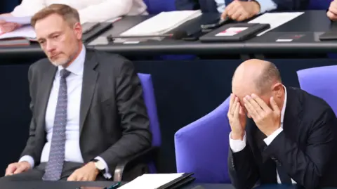 Shutterstock Finance Minister Christian Lindner and Chancellor Olaf Scholz sat together. Lindner is wearing a suit and Scholz has his head in his hands. 