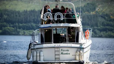 Getty Images A white boat called Nessie Hunter on Loch Ness. People sit on the top of the boat.