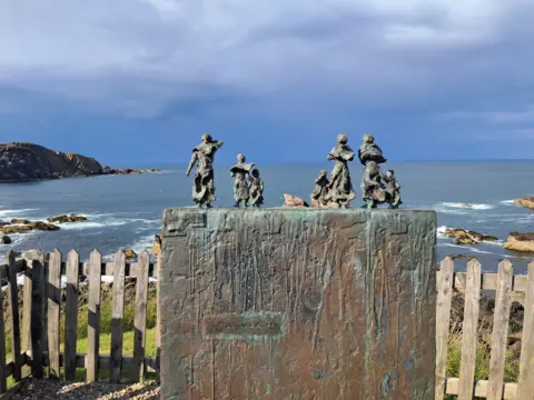 Rachel McGilvray A sculpture sitting overlooking the sea, with several small figures placed on it