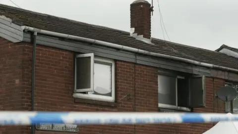 Burnt out window frames with police tape in the foreground at the crime scene.