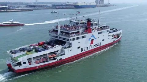 Red and white Red Funnel vehicle ferry sailing to the Isle of Wight a blue and white container ship can be seen at the docks in the background