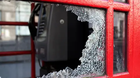 whitemay (via Getty Images) A red phone box with a shattered glass window 