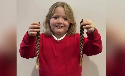 Kiera Moran  Noah smiling whilst holding two plaits of his hair up