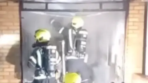 Jersey Fire and Rescue Service Two firefighters attend to a fire with two brick walls either side of an opening.