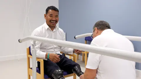 Jack Valpy/BBC A man with leg prosthetics is examined by someone in a white shirt. 