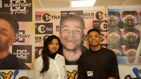 A teenage girl with long black hair wearing a white shirt next to a man with short black hair and a black t shirt.